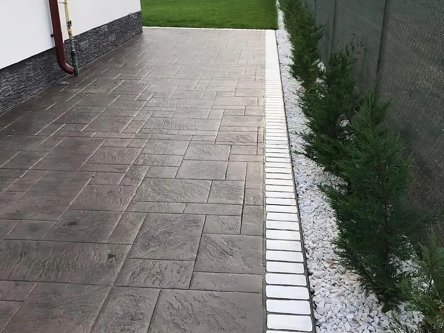 Gartenweg aus grauem Prägebeton mit sauberer Kante zwischen Rasen und Hausmauer