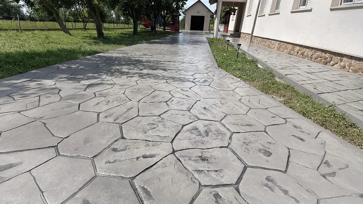 Breiter Gartenweg aus grauem Prägebeton in Bruchsteinoptik entlang eines Wohnhauses