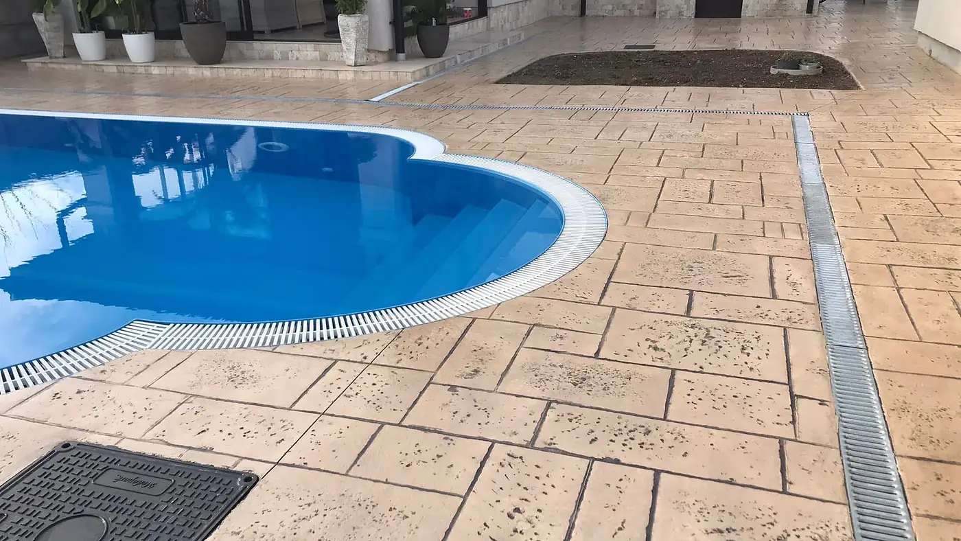 Poolumrandung aus sandbeigem Prägebeton mit Entwässerungsrinne und Plattenstruktur