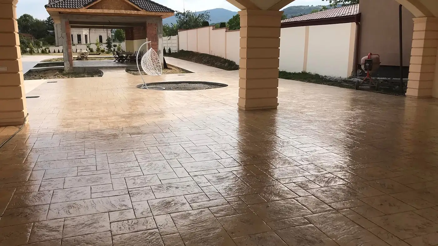 Überdachter Vorplatz aus braunem Prägebeton, Blick durch zwei Rundbögen in den Garten
