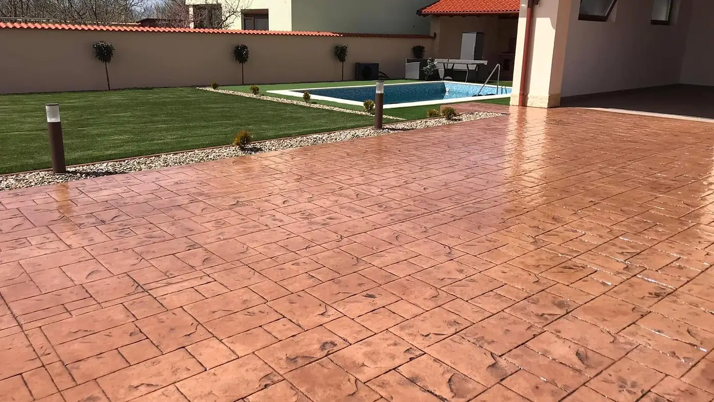 Grosse Hoffläche aus Prägebeton in Terracotta, dahinter Rasen und Schwimmbecken
