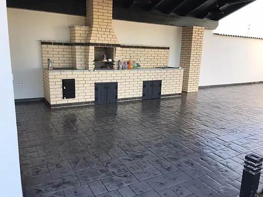 Überdachte Aussenküche mit Grillkamin auf anthrazitfarbenem Prägebeton