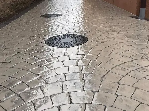 Gehweg im Fächerpflaster-Muster, grau, mit sauber eingepasstem Schachtdeckel