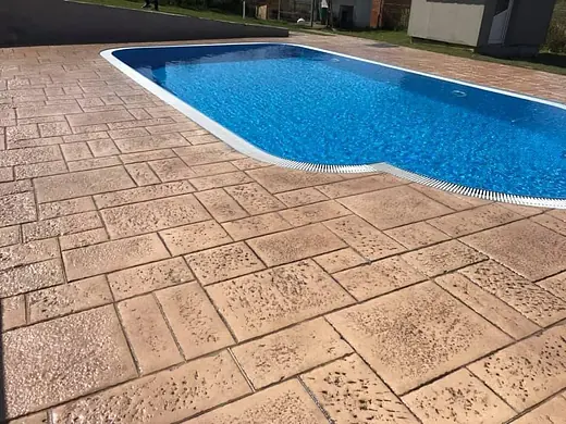 Grosszügige Poolfläche aus hellem Prägebeton mit Liegebereich