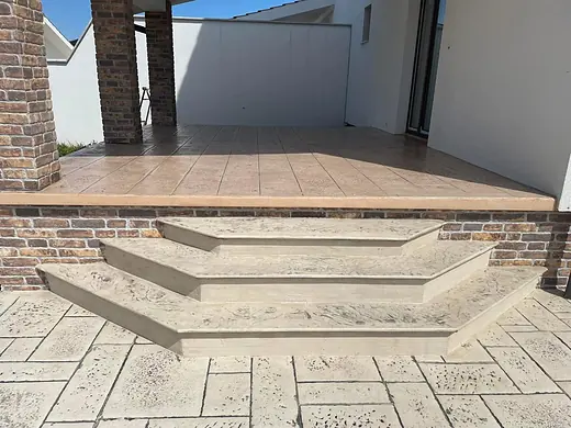 Überdachte Terrasse aus beigem Prägebeton mit drei Stufen und Ziegeleinfassung