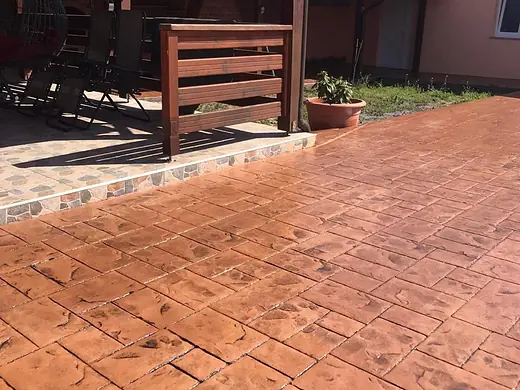 Terrasse aus terracottafarbenem Prägebeton unter einer Holzpergola