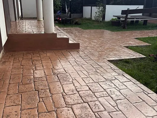 Sitzplatz aus terracottafarbenem Prägebeton neben Hauseingang und Säulen