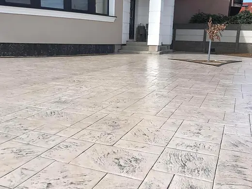 Heller Vorplatz aus Prägebeton im Plattenmuster vor einem modernen Neubau