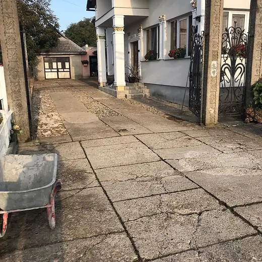 Alter Betonhof mit tiefen Rissen und Grasbewuchs vor der Sanierung